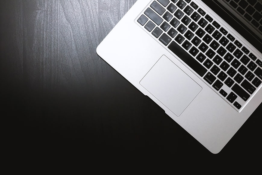 Silver laptop keyboard and trackpad on dark wooden desk