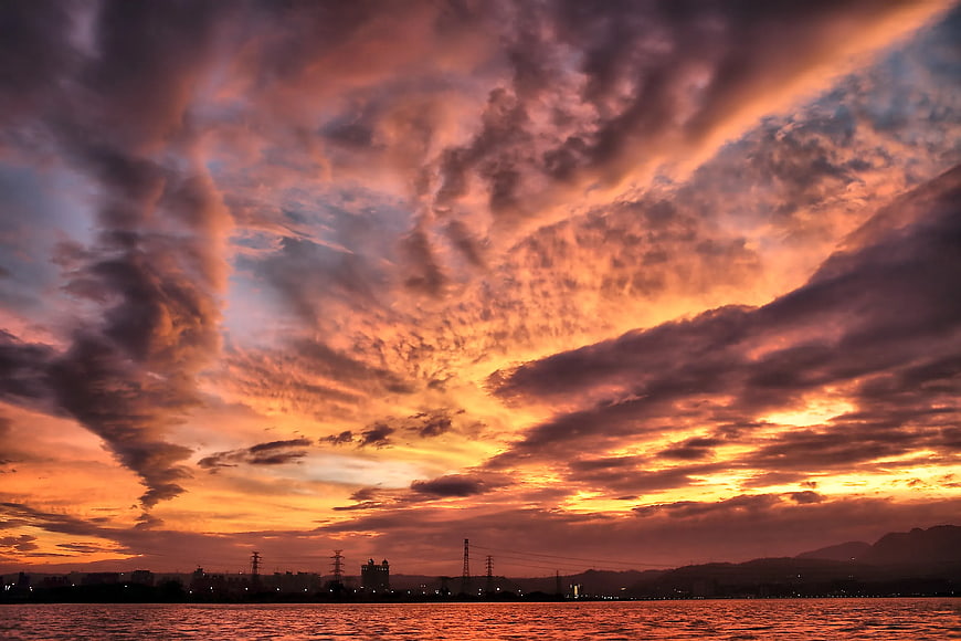 Dramatic orange and purple sunset clouds over water and city skyline