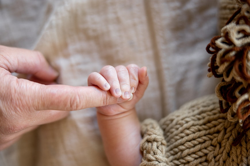 Close-up of newborn baby holding adult finger