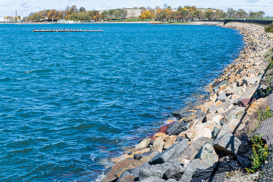 Rowing Team on Blue Water Near Rocky Shoreline