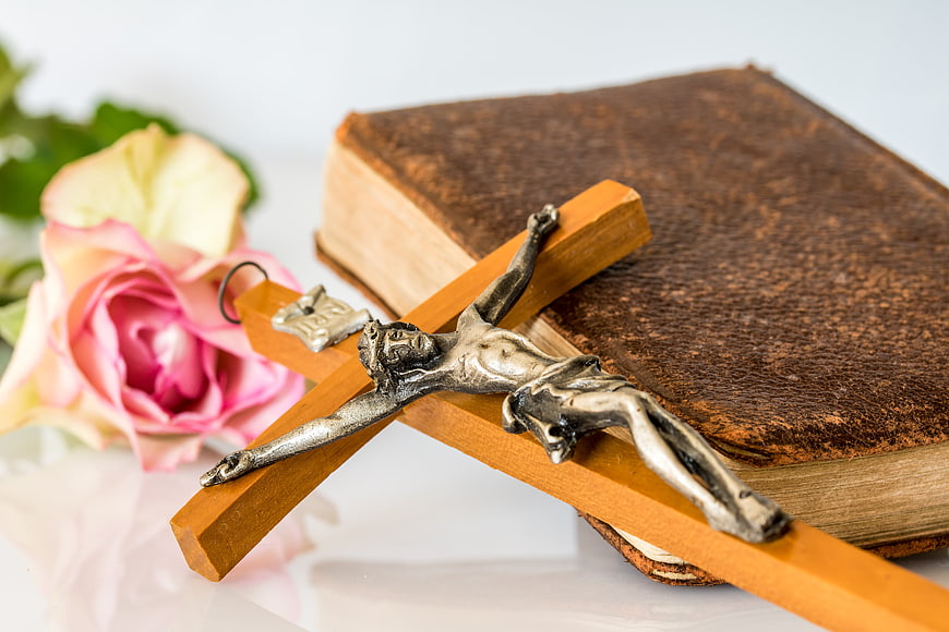 Wooden crucifix with silver Jesus figure on vintage book and pink rose