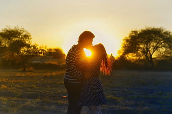 Silhouette of couple kissing in field at sunset
