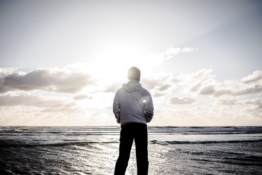 Man standing on beach looking at ocean sunset