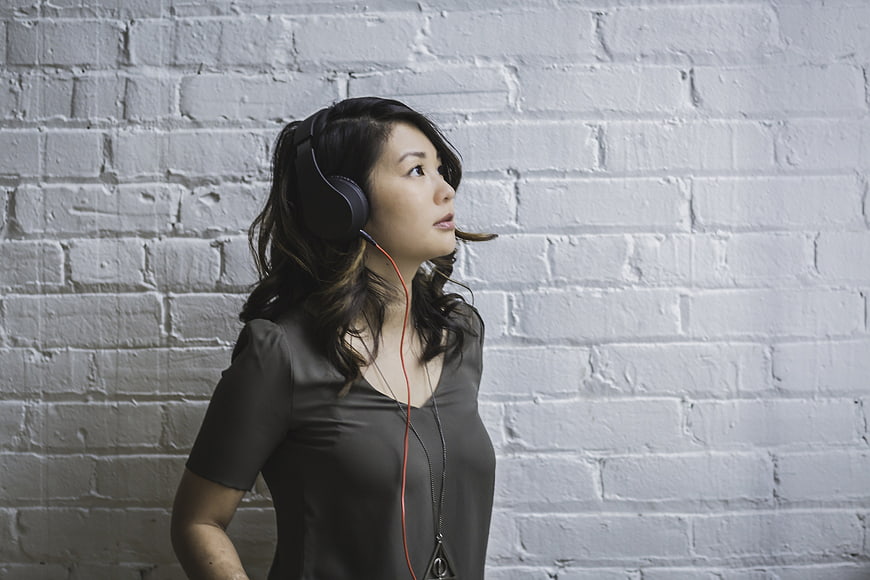 Woman with Headphones Listening to Music Against White Brick Wall