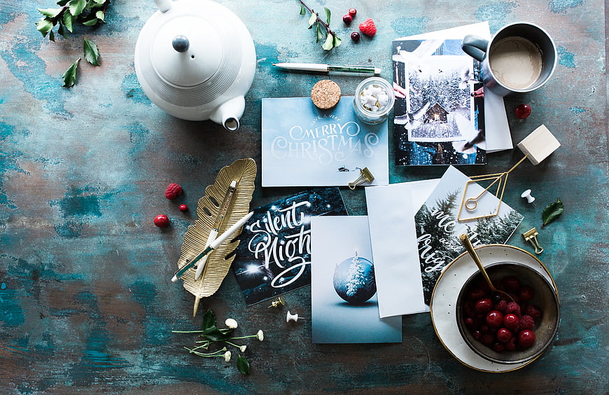 Flat lay of Christmas cards, teapot, and berries on blue table