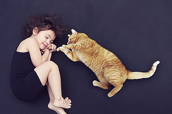 Sleeping child and orange tabby cat on dark background