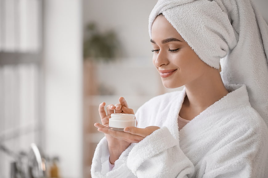Woman with towel on head holding skincare cream jar