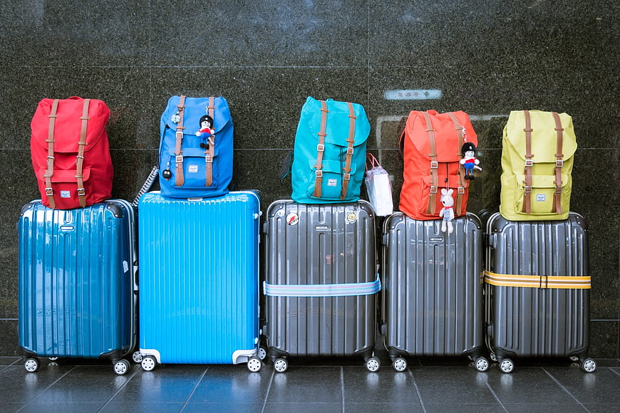 Colorful backpacks stacked on suitcases against a dark wall