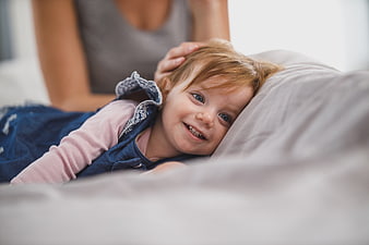 Smiling Toddler Girl Lying on Bed with Mother