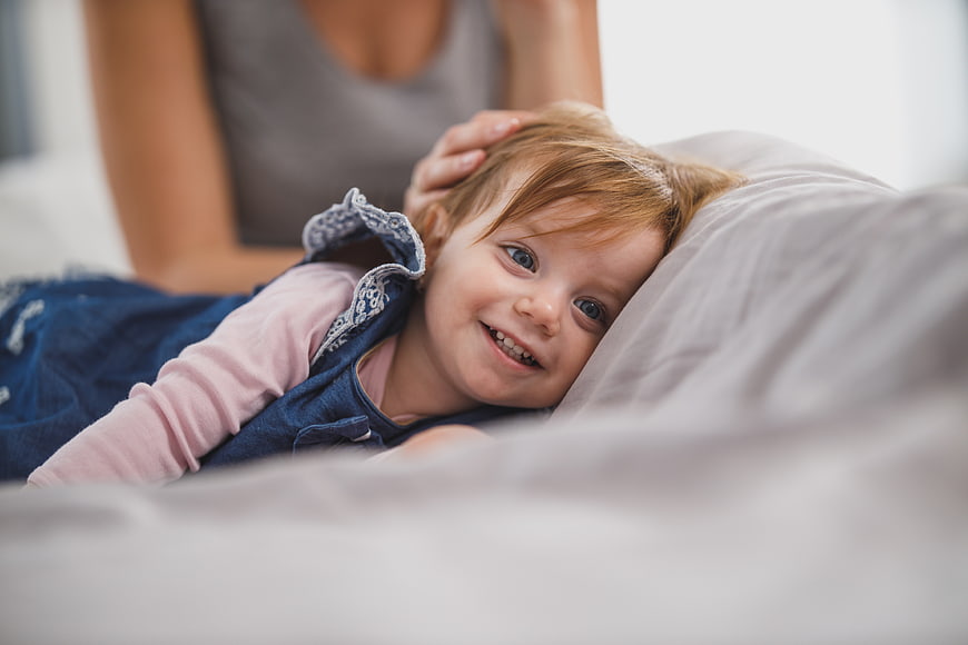 Smiling Toddler Girl Lying on Bed with Mother
