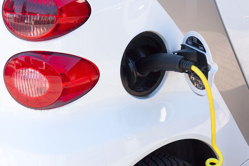 Close-up of white electric car charging with yellow cable