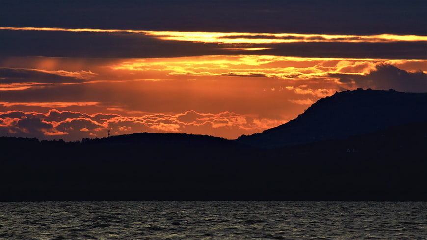 Dramatic Orange Sunset Over Silhouetted Hills and Lake