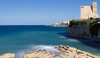 Historic stone tower on rocky Mediterranean coastline with blue sea