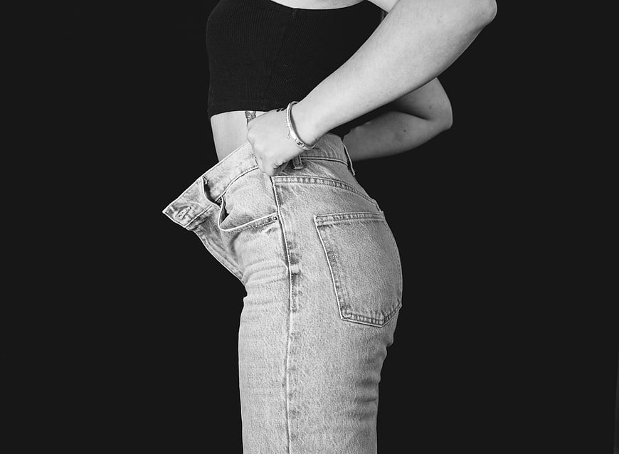 Woman in oversized jeans showing weight loss transformation
