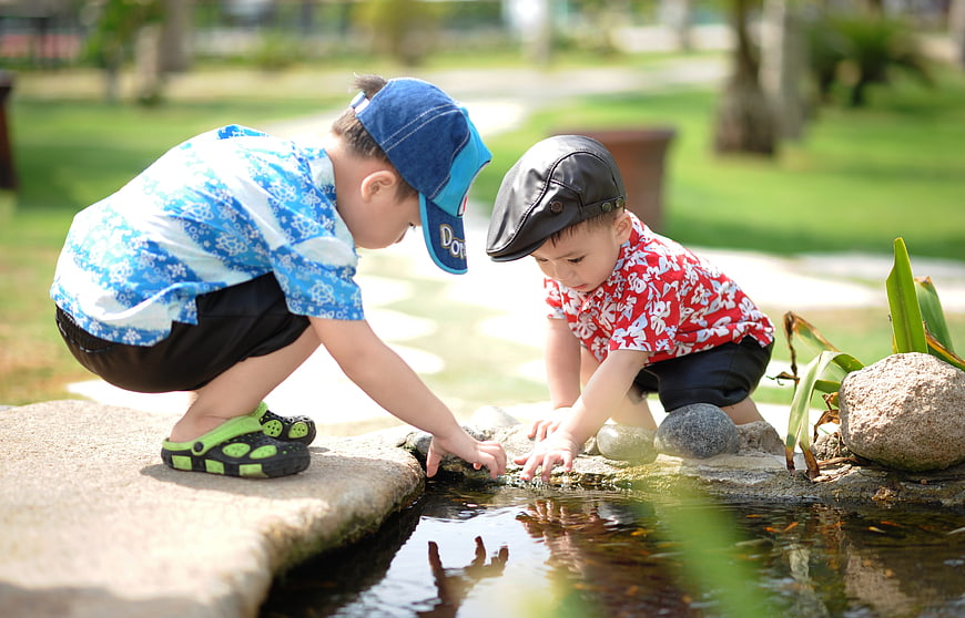 Two young boys playing in a park pond
