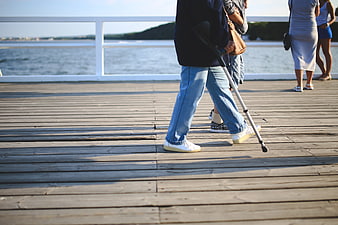 Person with crutch walking on wooden pier by the sea