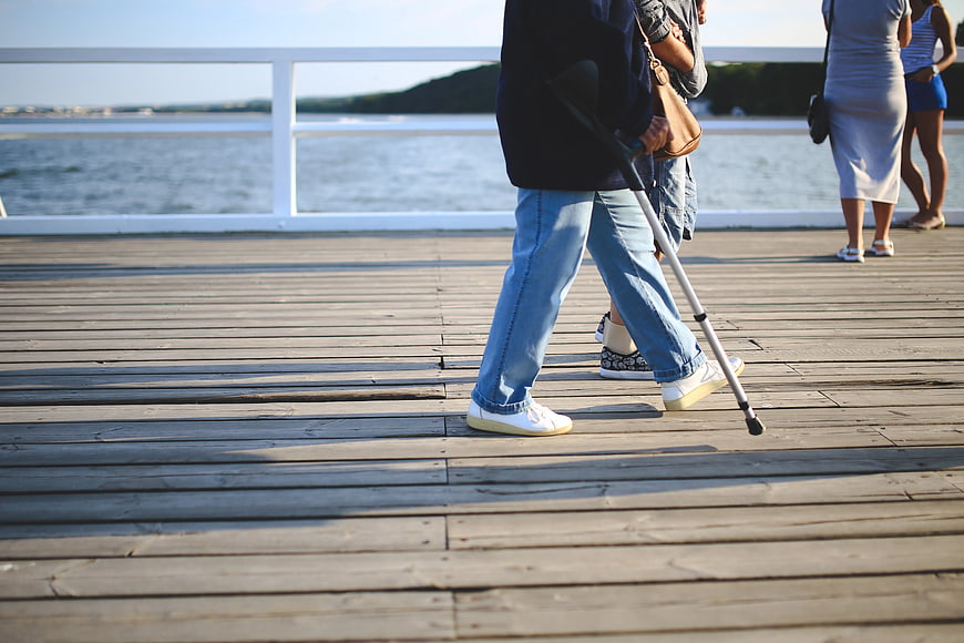 Person with crutch walking on wooden pier by the sea