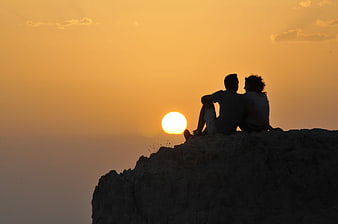 Silhouette of couple watching sunset on rocky cliff