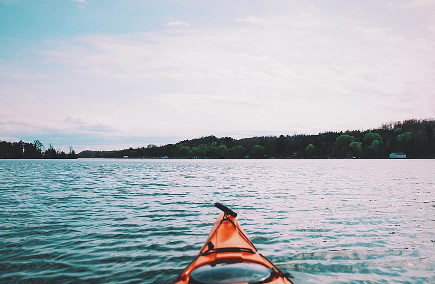 Orange Kayak on Calm Lake with Forest Shoreline