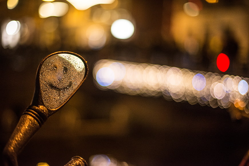 Smiley face reflection in scooter mirror with bokeh lights