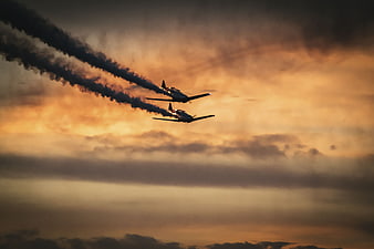 Two vintage warplanes flying in formation at sunset with smoke trails