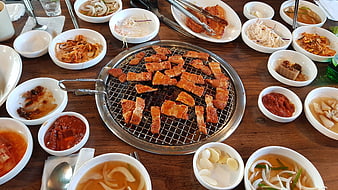 Korean BBQ pork belly on grill with assorted side dishes