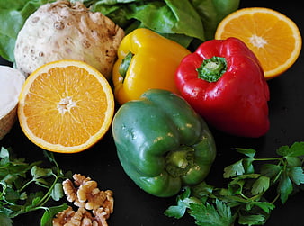 Fresh colorful bell peppers, oranges, and vegetables on black background