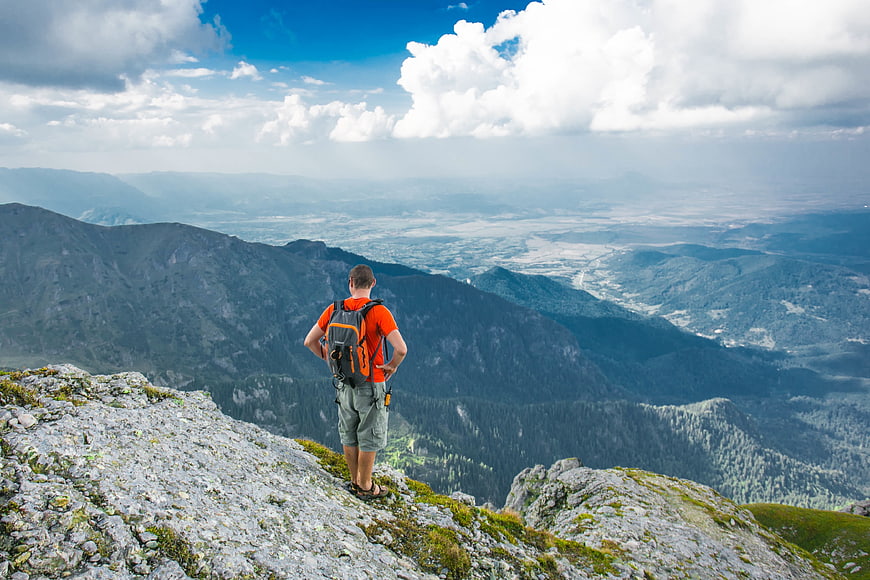 Hiker standing on mountain peak overlooking vast valley landscape