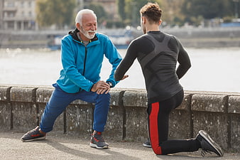 Senior and young man stretching together outdoors by river