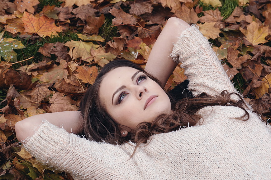 Young Woman Lying in Autumn Leaves Wearing Beige Sweater