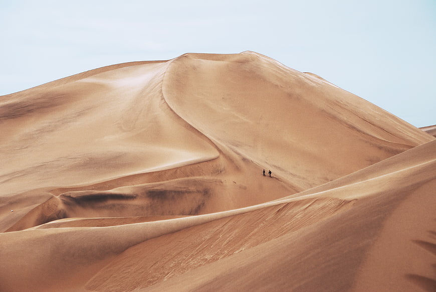 Two Hikers Walking on Massive Sand Dunes in Desert