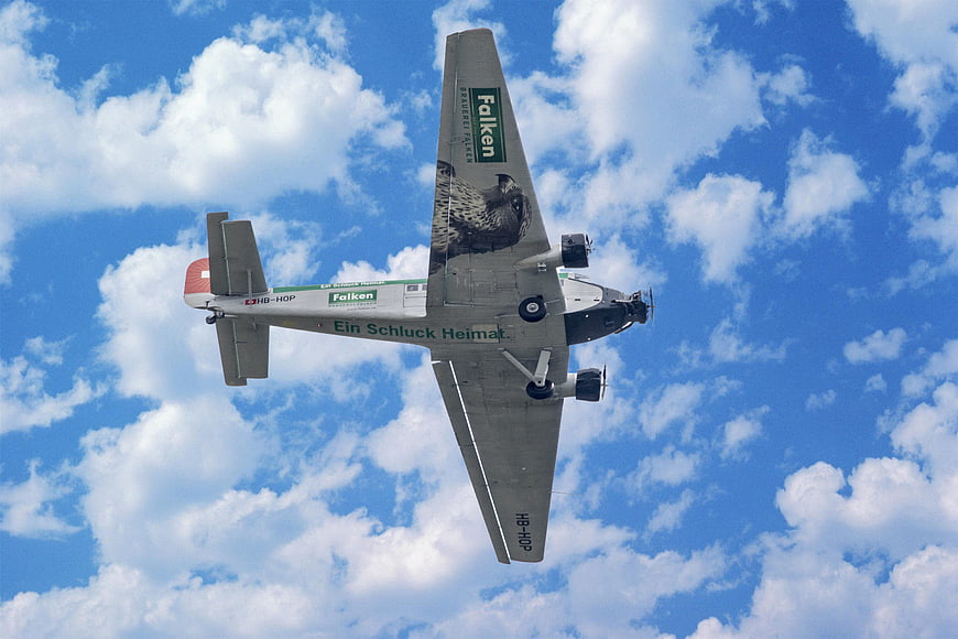 Vintage Twin-Engine Airplane Flying Against Blue Sky with Clouds