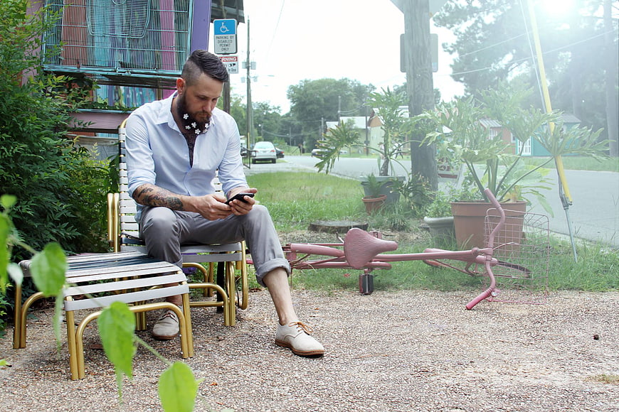 Stylish man with beard sitting on bench using smartphone outdoors