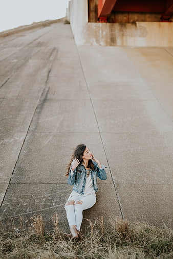Woman in denim jacket sitting on concrete embankment
