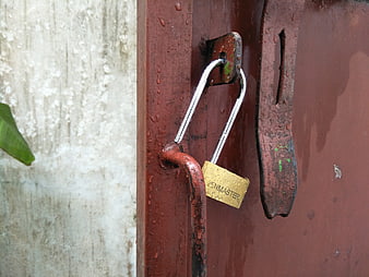 Close-up of brass padlock on rusty red metal gate with raindrops