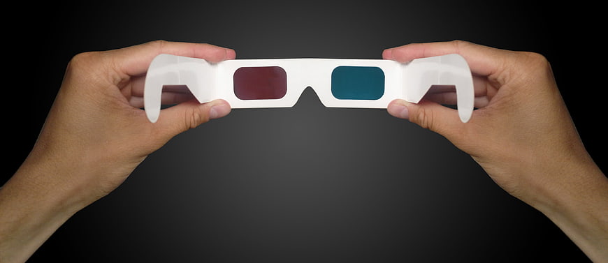 Hands Holding White Anaglyph 3D Glasses Against Dark Background