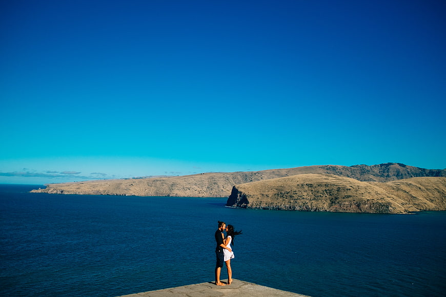 Couple kissing on cliff overlooking blue ocean and mountains