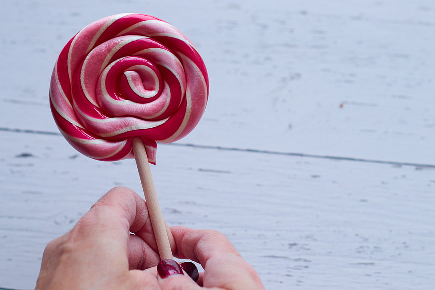 Hand holding pink and white swirled lollipop on white wood