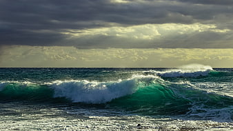 Powerful turquoise ocean wave crashing under dramatic cloudy sky