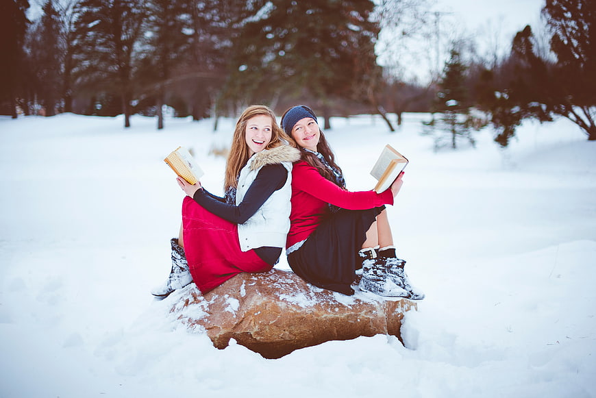 Two Happy Women Reading Books Back to Back in Snow