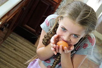 Young Girl Holding Brown Egg in Kitchen