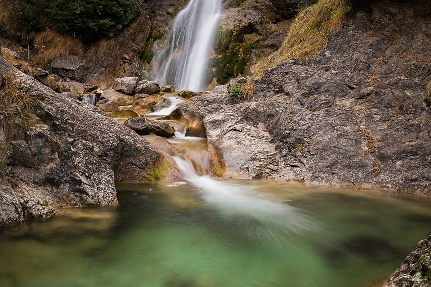 Serene Mountain Waterfall Cascading Over Rocks into Green Pool
