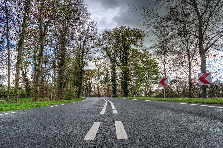 Winding asphalt road through forest with traffic signs