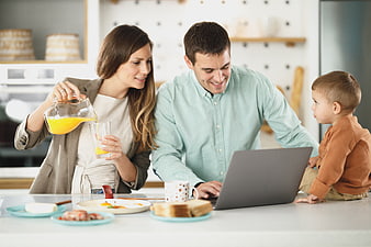 Happy family having breakfast while father works on laptop