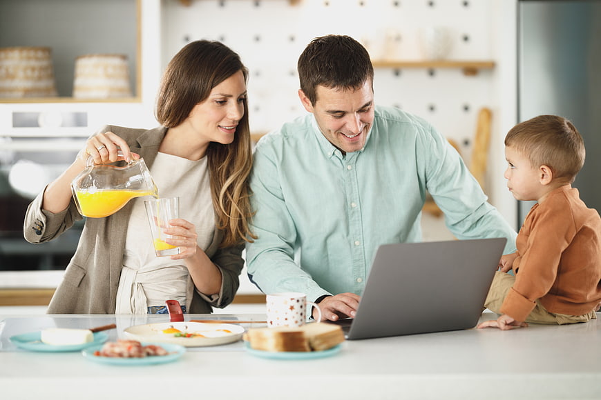 Happy family having breakfast while father works on laptop
