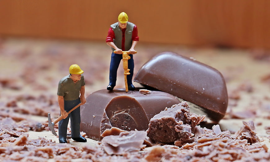 Miniature construction workers mining chocolate bar