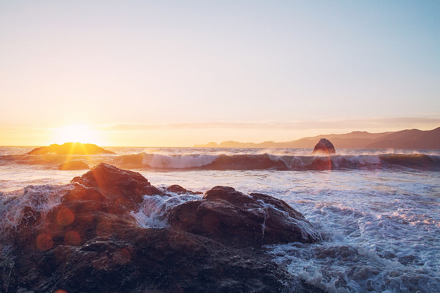 Sunset over rocky ocean waves with distant mountains