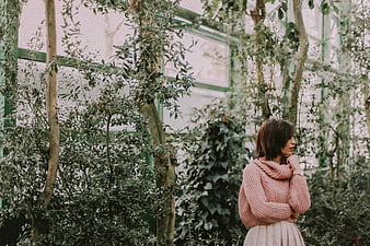 Woman in Pink Sweater Standing in Lush Greenhouse Garden