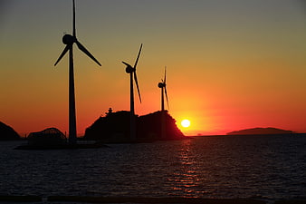Silhouetted wind turbines at sunset over the ocean