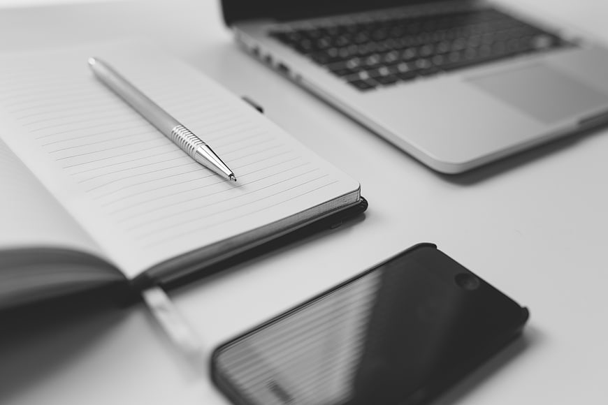 Black and white workspace with notebook, pen, laptop, and smartphone